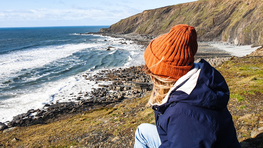 a woman sitting on a cliff overlooking the ocean