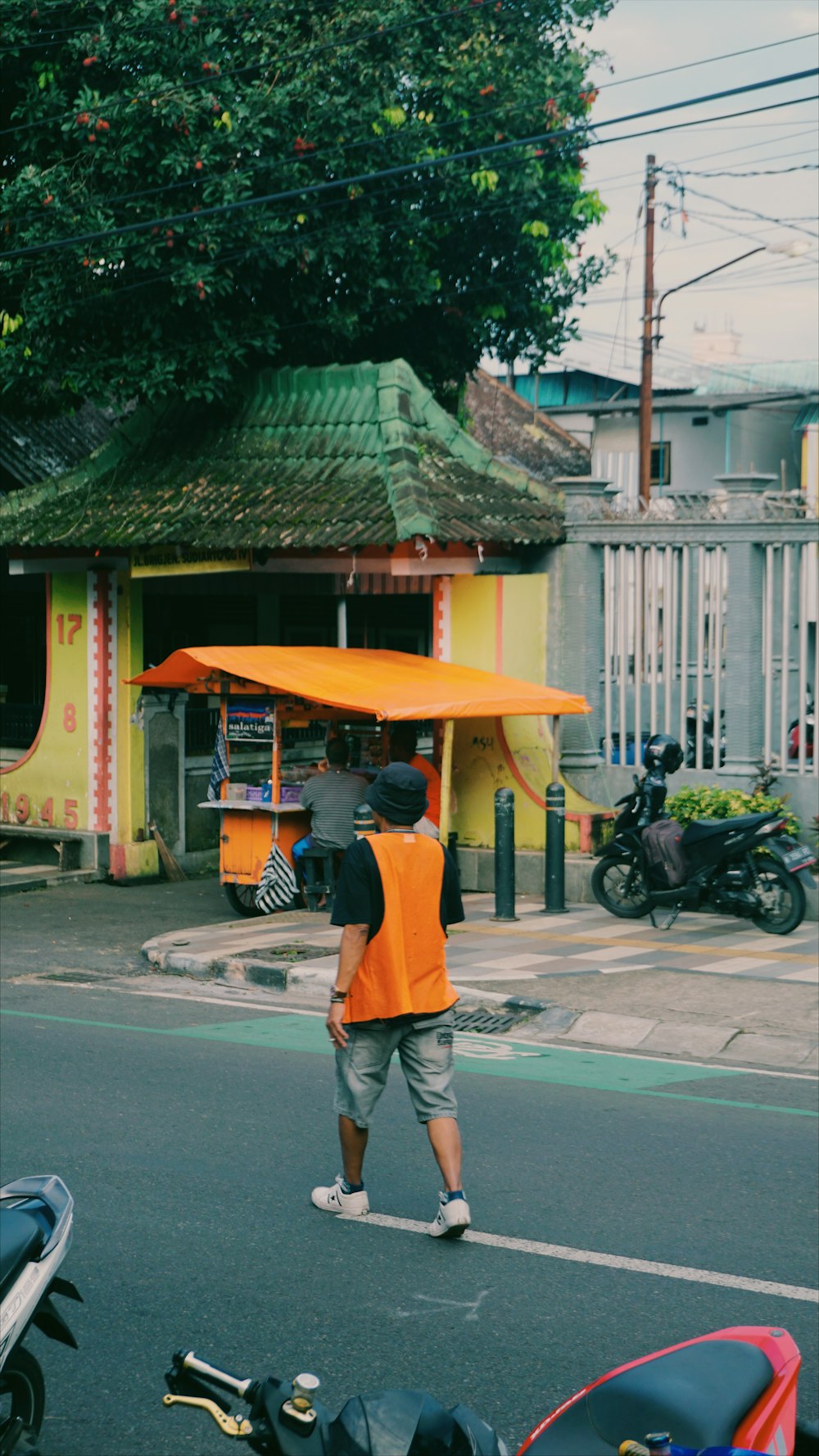 a man in an orange vest walking down a street