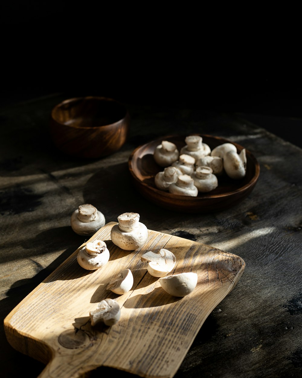 uma tábua de corte de madeira coberta com cogumelos ao lado de uma tigela de cogumelos