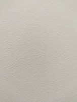 A smooth, light-colored wall texture with subtle variations in tone and slight imperfections visible on the surface.