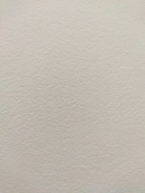 A smooth, light-colored wall texture with subtle variations in tone and slight imperfections visible on the surface.