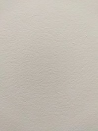 A smooth, light-colored wall texture with subtle variations in tone and slight imperfections visible on the surface.