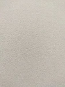 A smooth, light-colored wall texture with subtle variations in tone and slight imperfections visible on the surface.