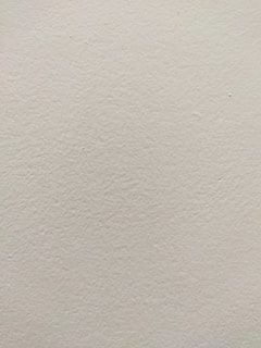 A smooth, light-colored wall texture with subtle variations in tone and slight imperfections visible on the surface.