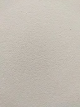 A smooth, light-colored wall texture with subtle variations in tone and slight imperfections visible on the surface.
