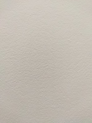 A smooth, light-colored wall texture with subtle variations in tone and slight imperfections visible on the surface.