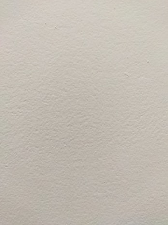 A smooth, light-colored wall texture with subtle variations in tone and slight imperfections visible on the surface.