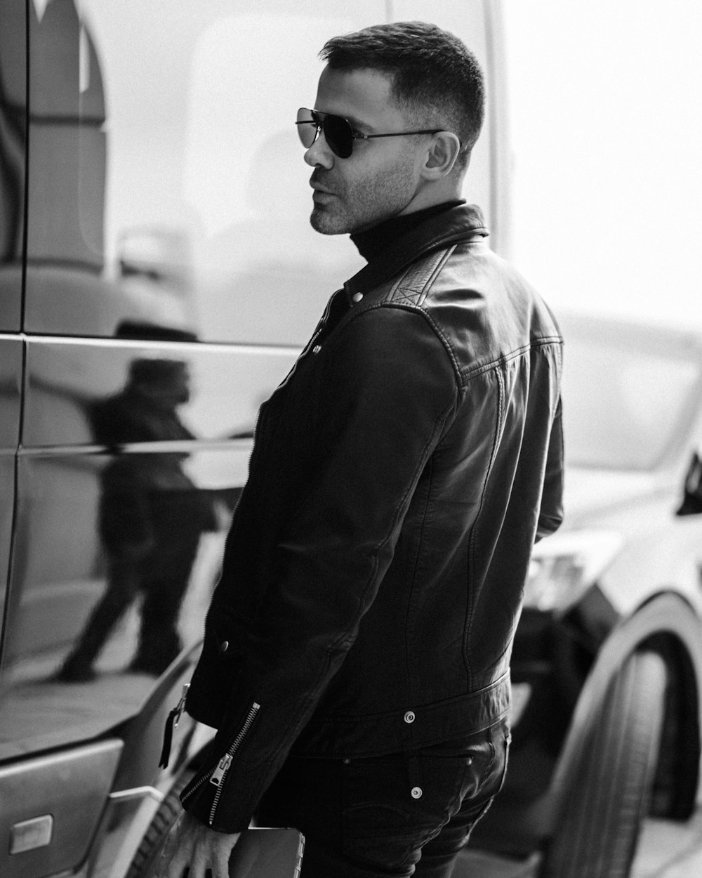 a man in a leather jacket and sunglasses standing next to a car