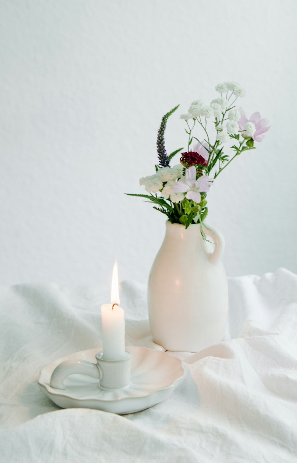 a white vase filled with flowers next to a lit candle