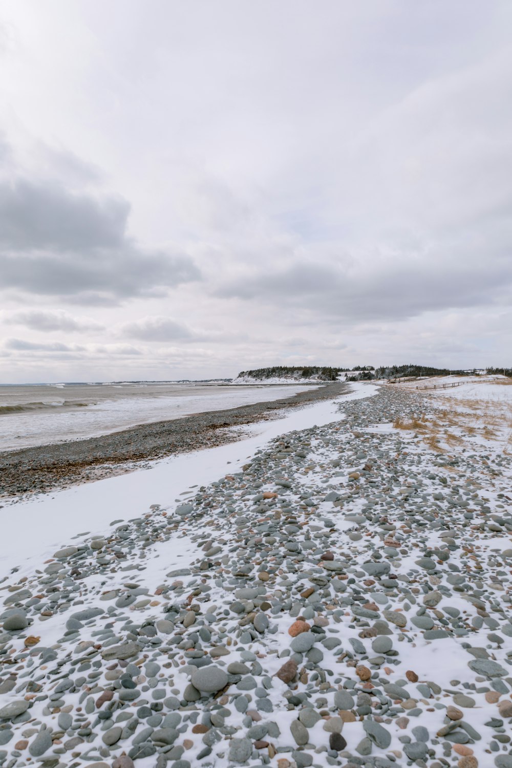 a rocky beach covered in snow next to a body of water