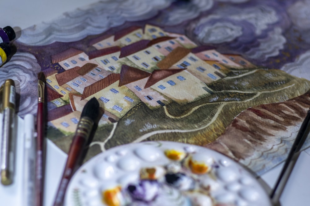 a table with a plate of food and paint brushes