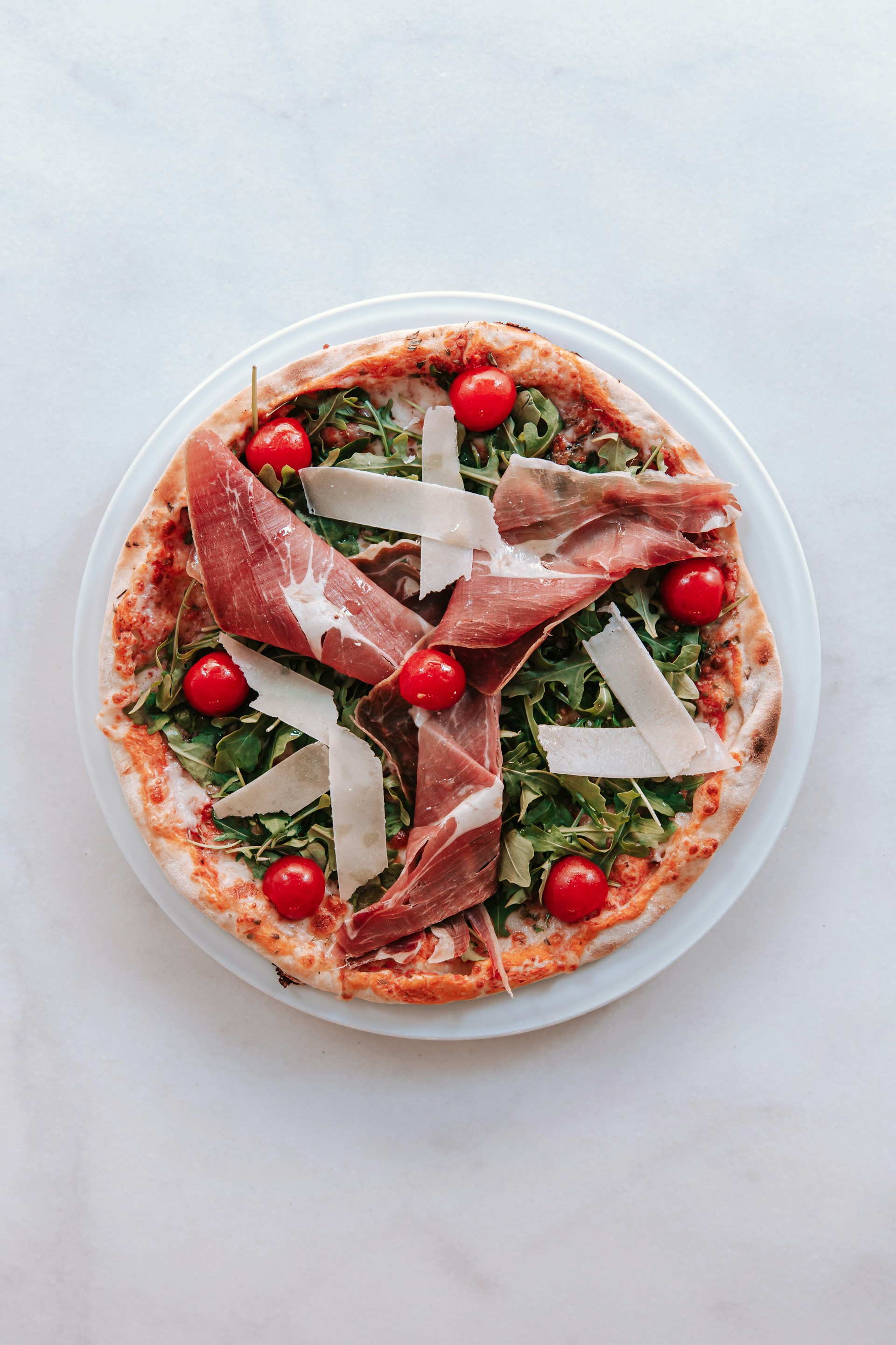 a pizza topped with prosciutto and cheese on a white plate