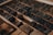A collection of vintage printing blocks arranged in a drawer, showing various letters and numbers made from dark wood or metal. These blocks are set in rows, showcasing the intricacies of old-school typography used in traditional printing presses.