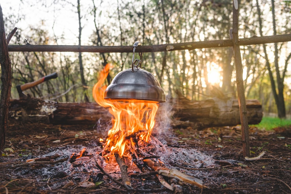 un feu brûlant dans une forêt avec un grand pot en métal sur le dessus