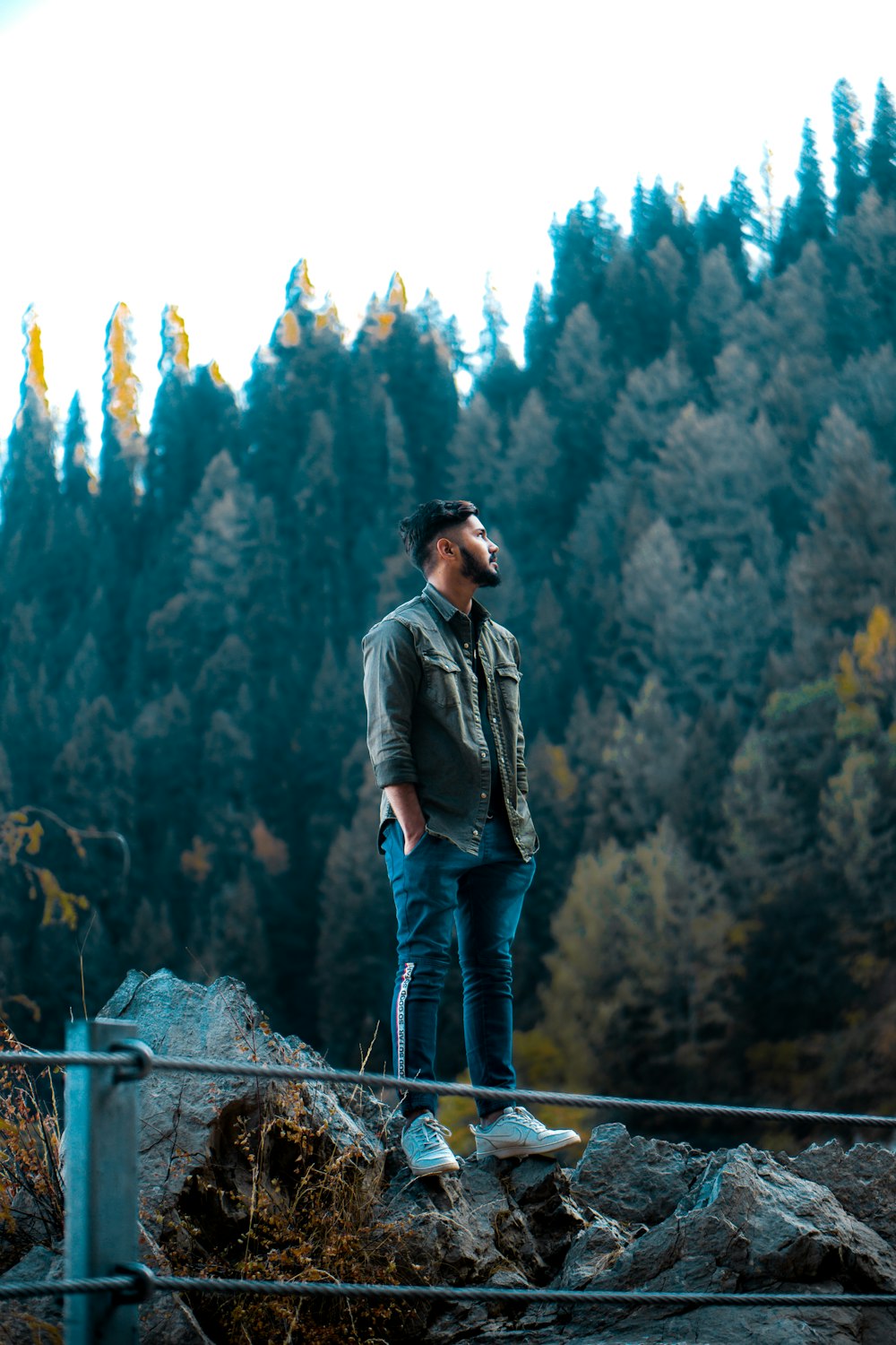 um homem em pé no topo de uma rocha ao lado de uma floresta