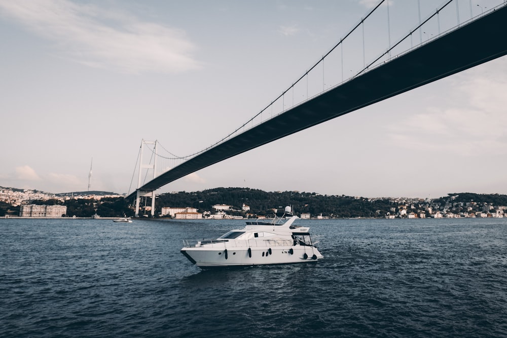 a white boat in the water under a bridge