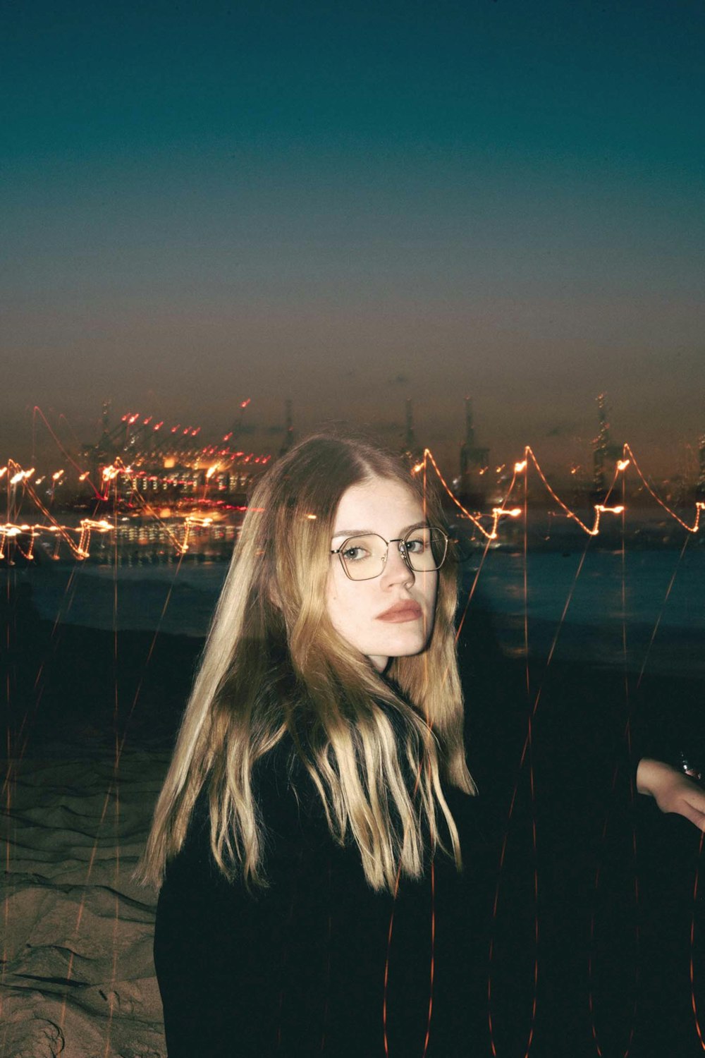 a woman with glasses standing on a beach at night