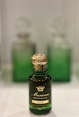 A green glass bottle of Marsoom Fragrance No. 2 with an ornate gold cap is prominently displayed. Behind it, two similar bottles are blurred, creating a sense of depth.