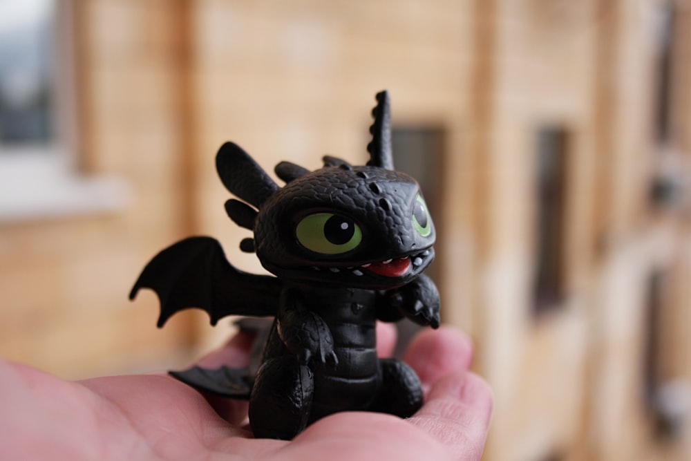 a small black toy with green eyes in a persons hand