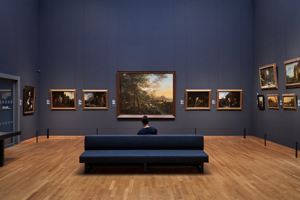 a person sitting on a blue couch in a museum