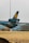 A UPS airplane is parked on an airfield, with its tail and engine visible. The aircraft has the UPS logo on its tail and is situated near an industrial building with containers in the background. The ground is covered with dry grass, indicating a possibly dry climate or season.