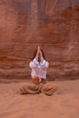 a woman in a white shirt and brown pants sitting in the sand