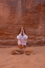 a woman in a white shirt and brown pants sitting in the sand