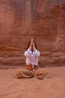 a woman in a white shirt and brown pants sitting in the sand