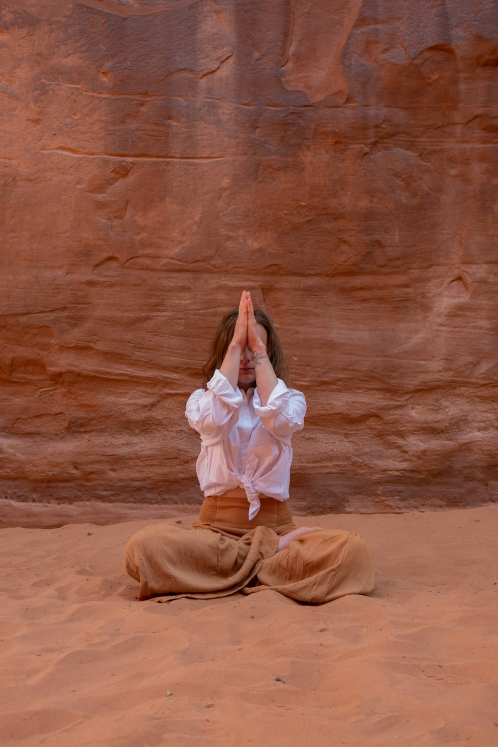 a woman in a white shirt and brown pants sitting in the sand