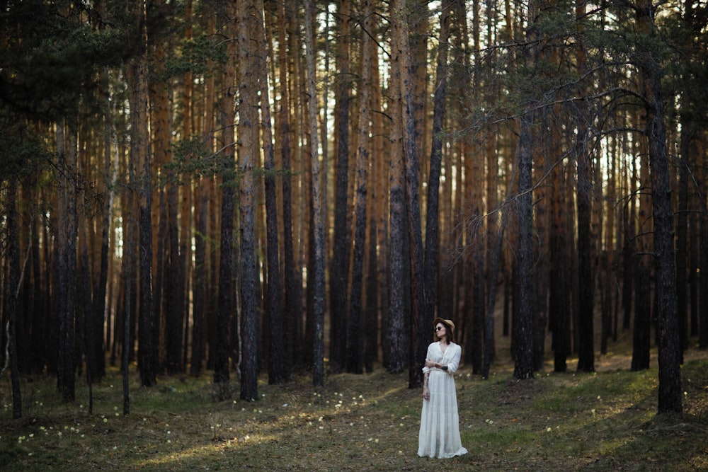 a woman in a white dress standing in a forest