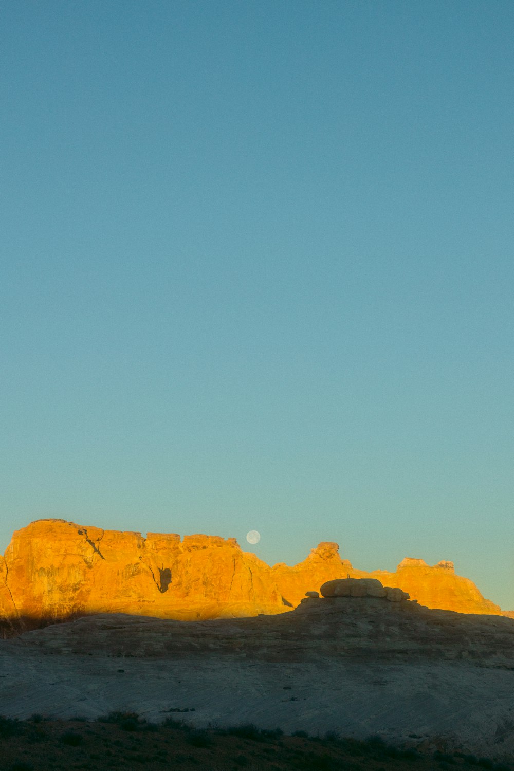 the moon is setting over the mountains in the desert