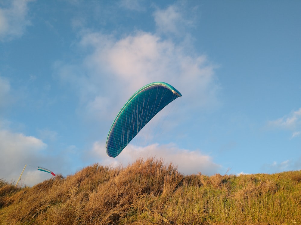 a paraglider flying over a grassy hill under a blue sky