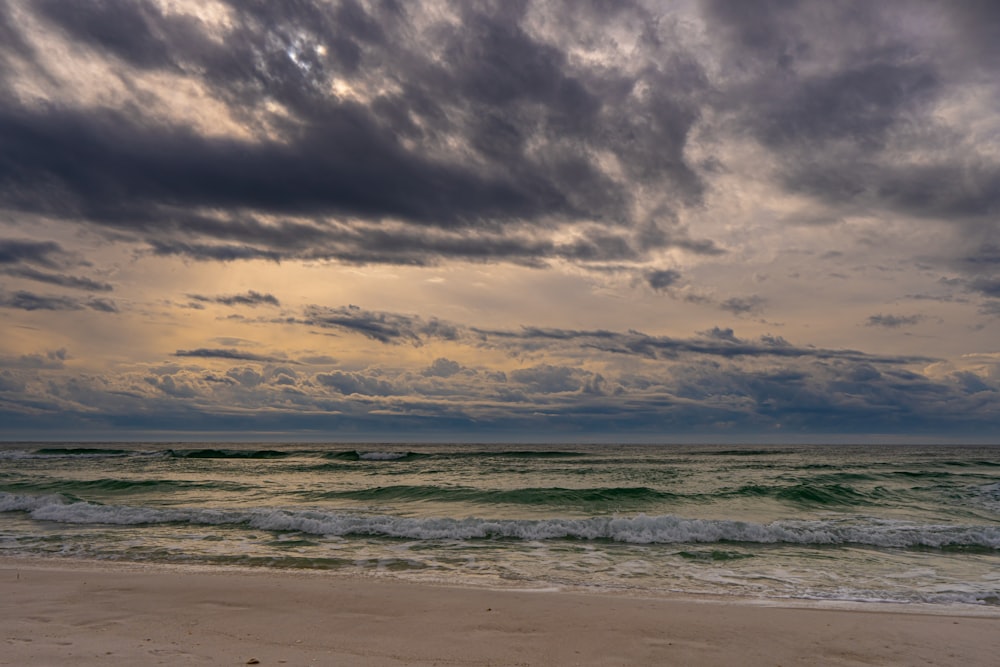 a cloudy sky over the ocean with waves coming in