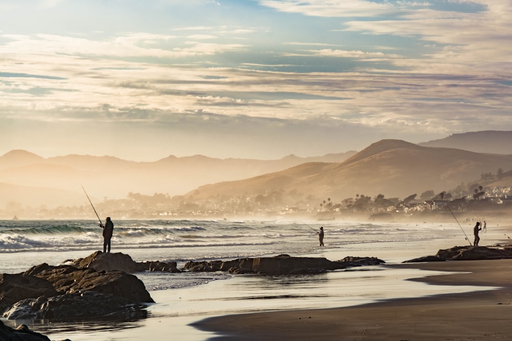 um par de pessoas em pé no topo de uma praia ao lado do oceano