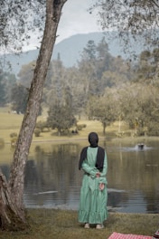 a woman standing next to a tree near a lake