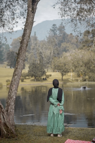 a woman standing next to a tree near a lake