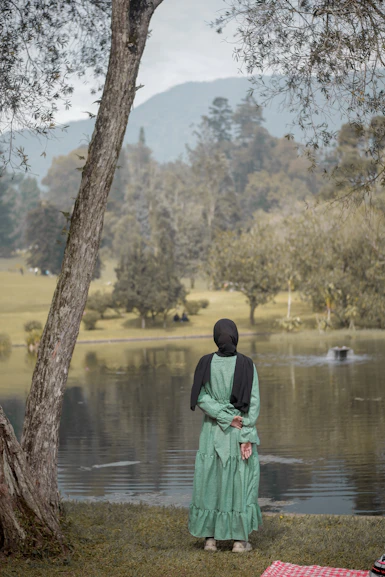 a woman standing next to a tree near a lake