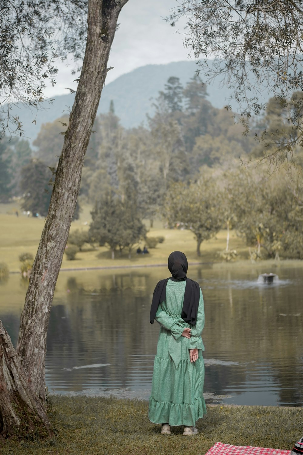 a woman standing next to a tree near a lake