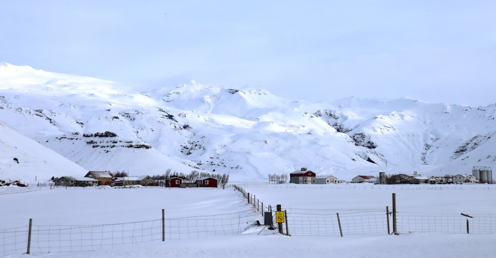 a snow covered field with a fence and mountains in the background