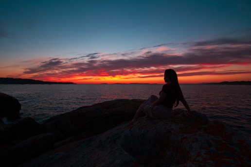 a woman sitting on top of a rock next to the ocean