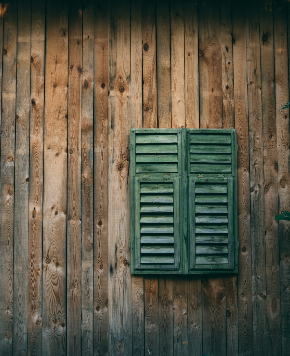 a green shuttered window on a wooden wall