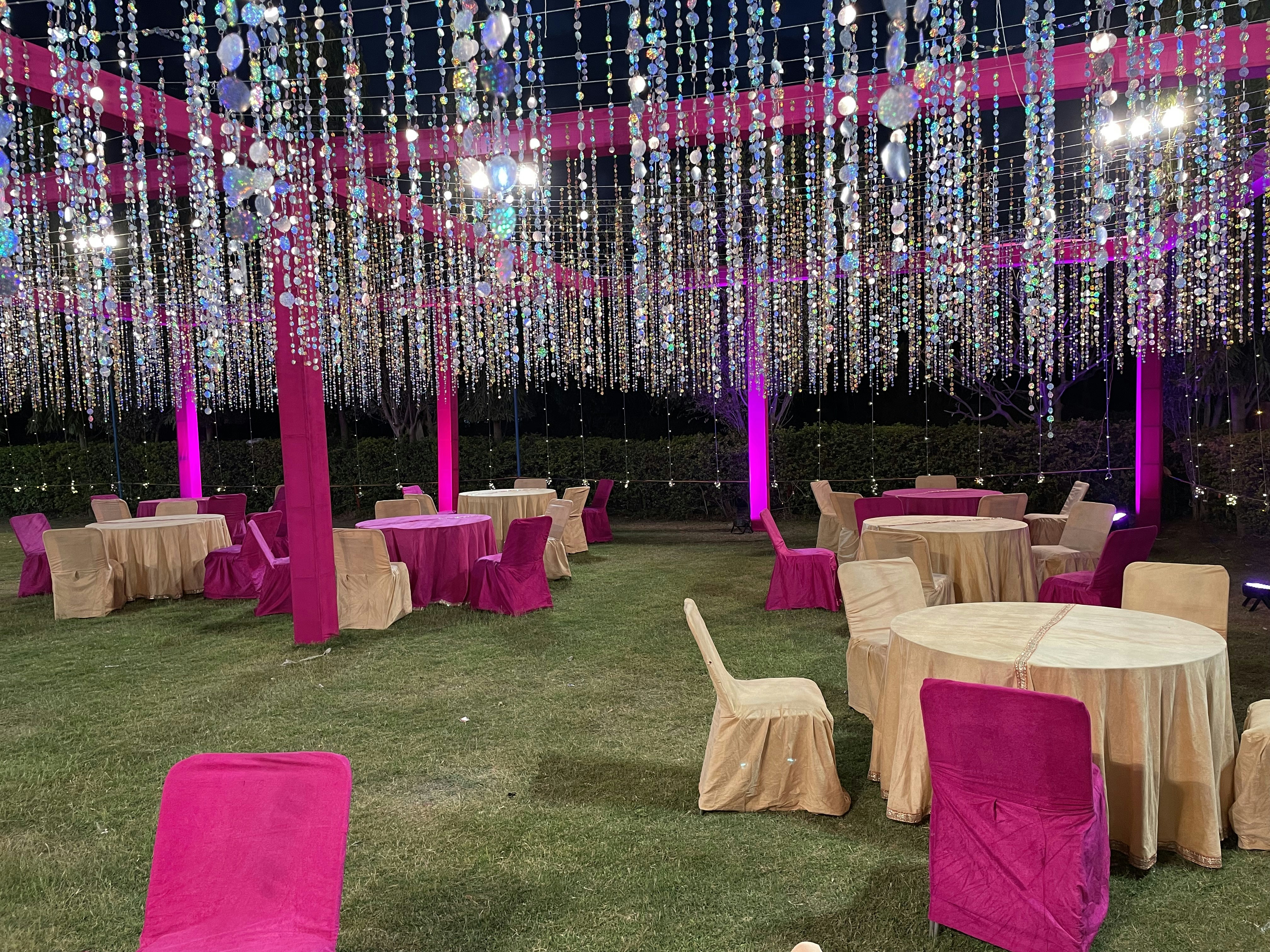Colorful party setup with balloon arch, tables decorated in pink and gold, bright festive venue, warm lighting