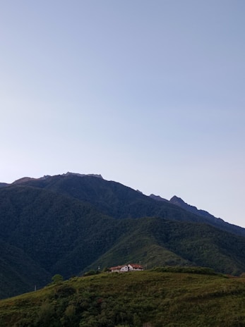 A serene hillside homestay surrounded by lush green mountains under a clear blue sky.