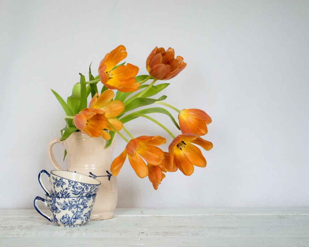 a vase filled with orange flowers next to a cup