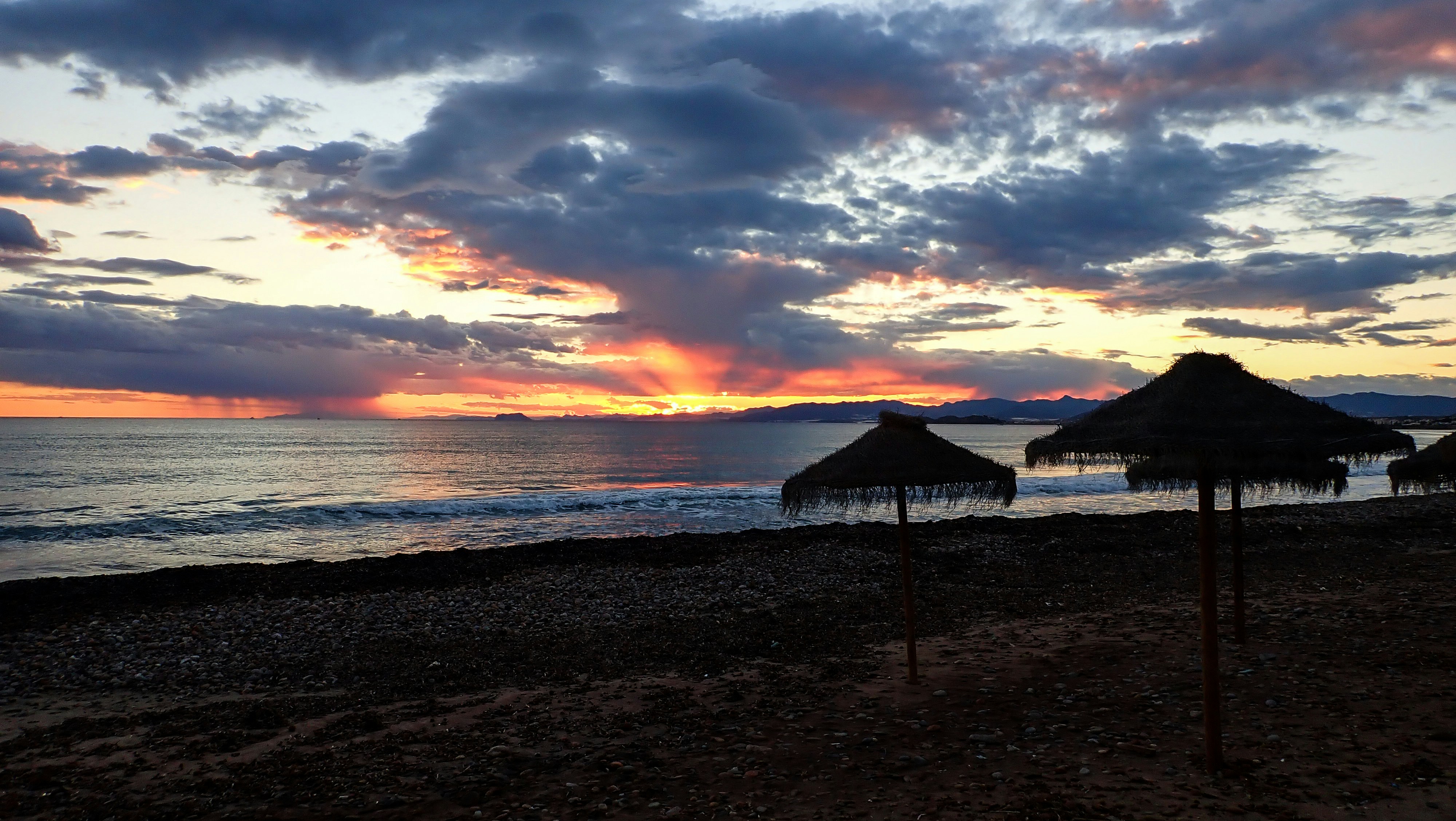 un tramonto su una spiaggia con ombrelloni in primo piano