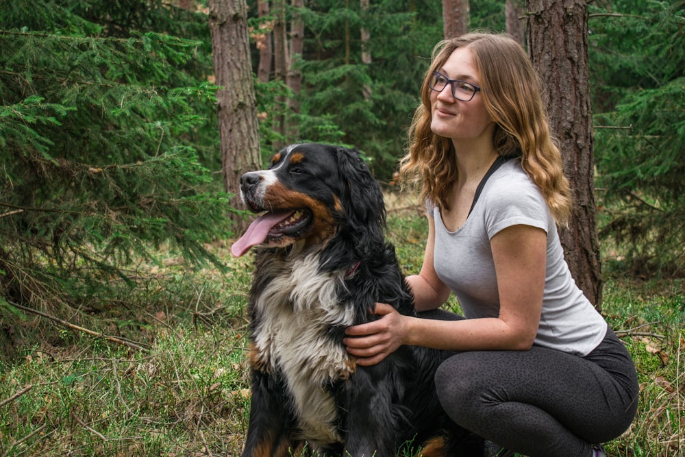 a woman kneeling down next to a dog in the woods