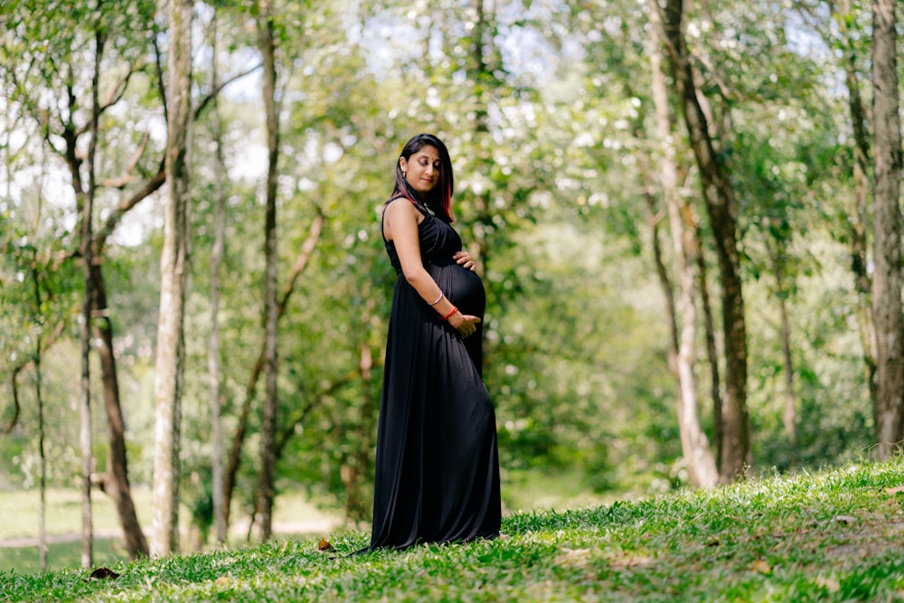 a pregnant woman in a black dress standing in the woods