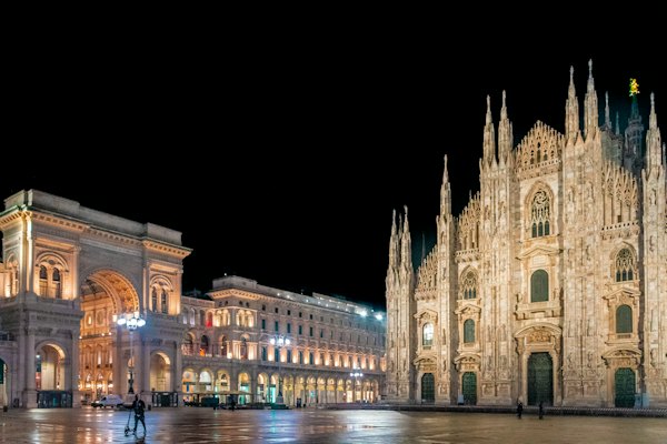 A cathedral lit up at night with people walking around — Milan, Italy