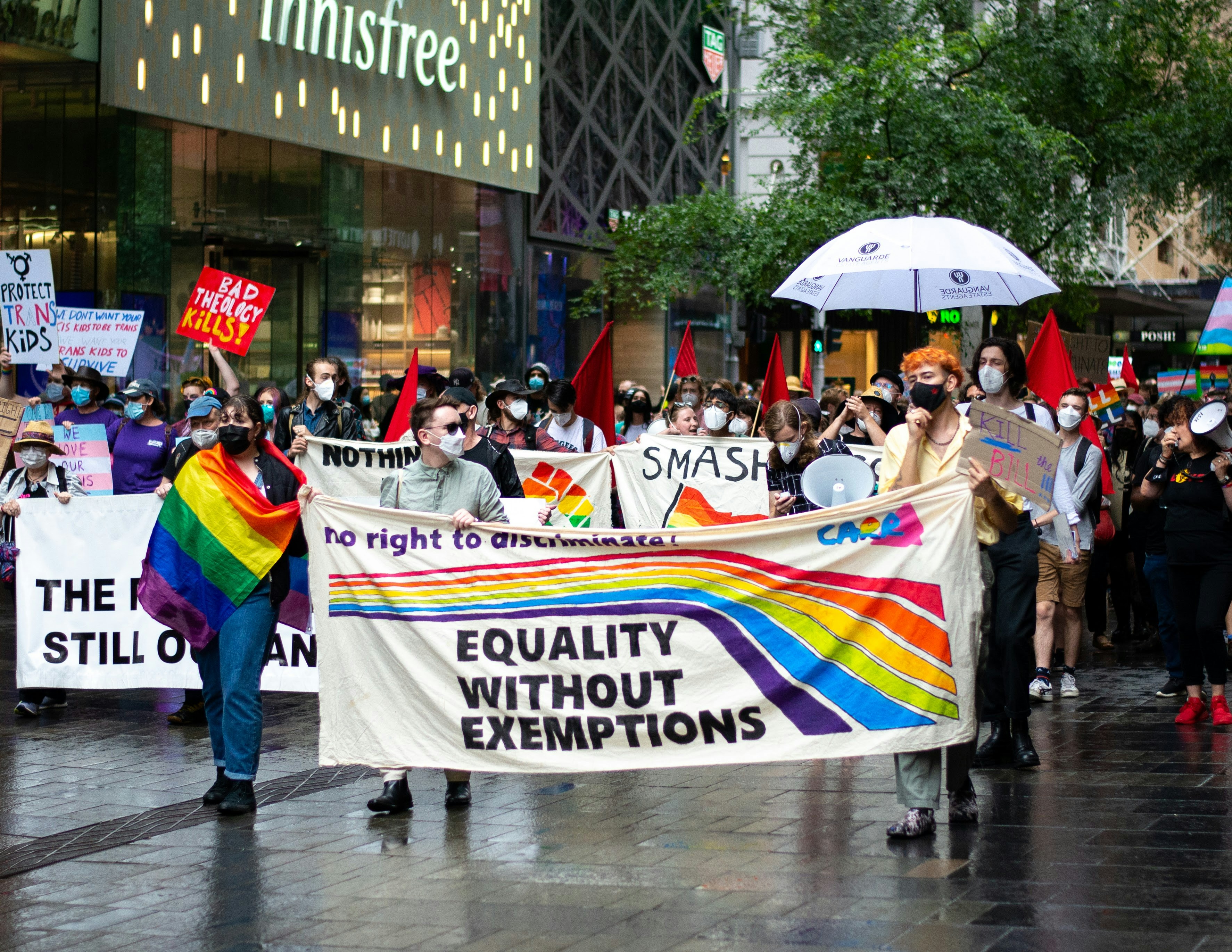 a group of people walking down a street holding a rainbow banner