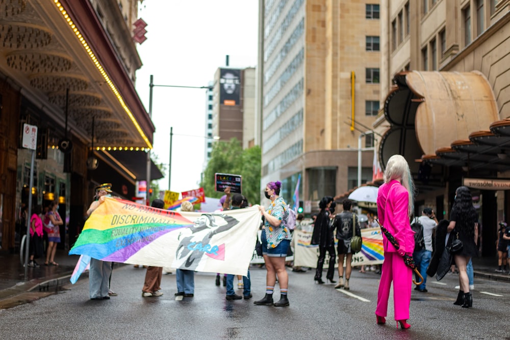 Un groupe de personnes marchant dans une rue tenant un drapeau arc-en-ciel